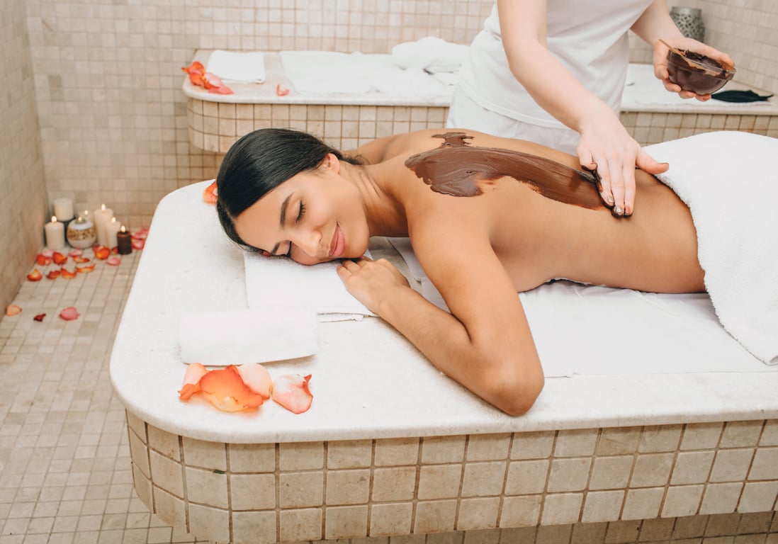 Mixed race woman having chocolate body mask in spa salon. Luxury resort and massage. Chocolate body scrub